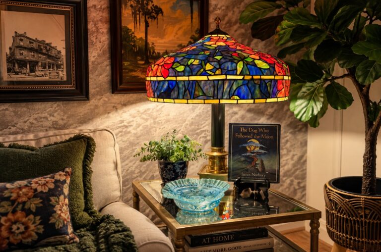 Large Tiffany-style lamp glowing in a collected living room filled with art, books and plants.